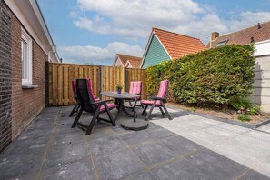 Eine Terrasse mit Tisch und Stühlen, ein Holzzaun und ein Hecke.