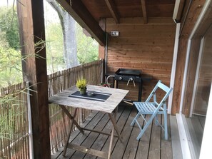 A wooden deck with a table and chairs, a grill, and a view of trees. - Perched studio apartment with a terrace overlooking the river—nature and tranquility near Nancy (Pulligny)