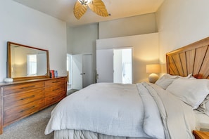 Quarto com uma cama grande, cômoda de madeira, espelho e ventilador de teto.