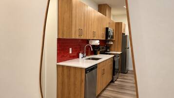 A modern kitchen with wooden cabinets, a red backsplash, and a stainless steel dishwasher.