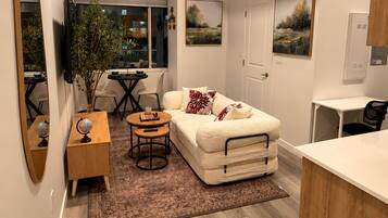 A compact living space with a sofa, a dining table, a small rug, and a mirror.