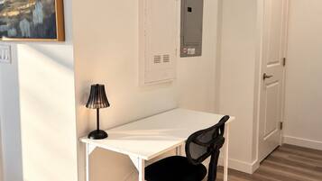 A white desk with a black office chair, a wall-mounted electrical panel, and a painting on the wall.