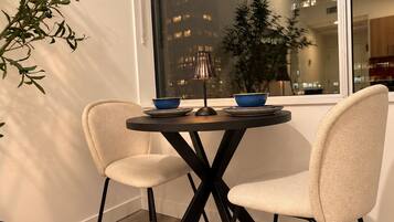 A dining area with a round table, two chairs, a lamp, and a window with a view of buildings.