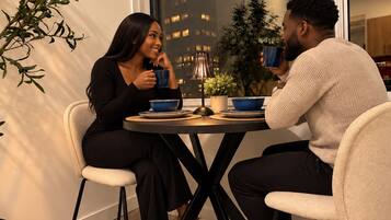 Two people seated at a table with a city view, a lamp, and a potted plant.