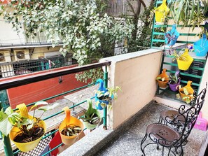 Ein Balkon mit Blumentöpfen, einem Metallstuhl und Blick auf die Straße.