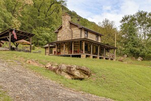 A rustic cabin with a stone chimney, a covered porch, and a flagpole. - Right on New River! Historic Cabin w/ Hot Tub (Prince)