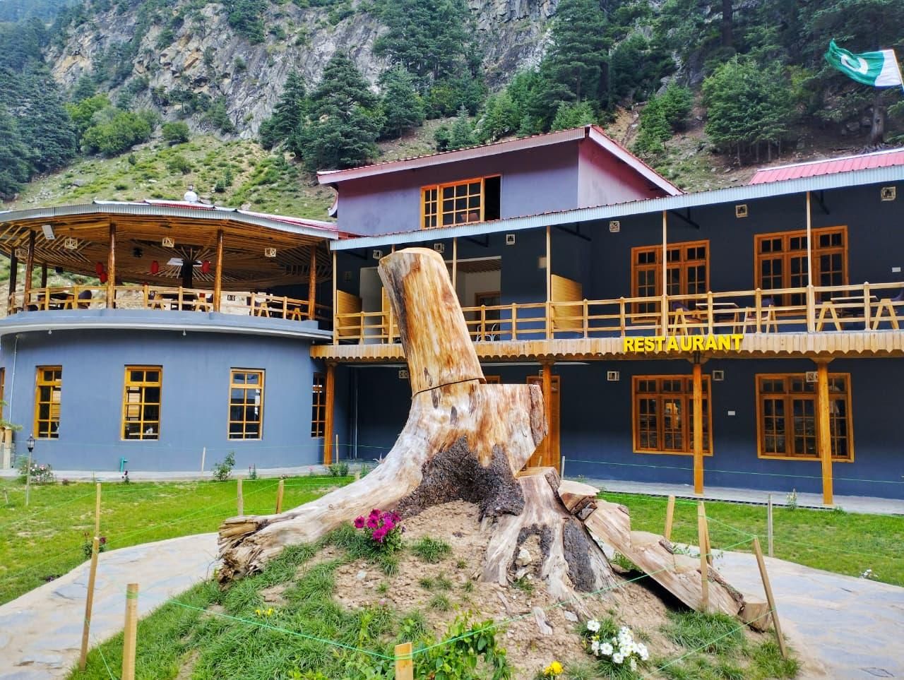 Un restaurant dont le décor est dominé par une grande souche d’arbre, le tout étant situé dans un paysage montagneux.