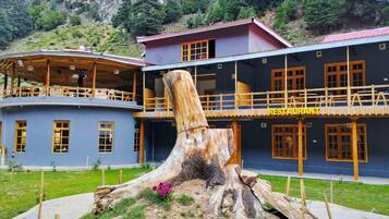 Un restaurant dont le décor est dominé par une grande souche d’arbre, le tout étant situé dans un paysage montagneux.