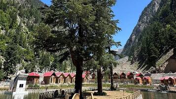 Un puente de madera que conduce a una hilera de cabañas con tejados rojos, rodeado de un paisaje montañoso y una masa de agua.