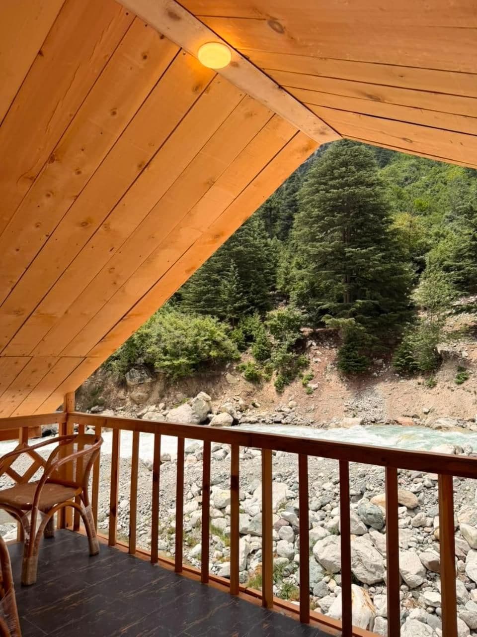 Una terraza de madera con barandilla que da a la ribera rocosa de un río y una ladera boscosa.