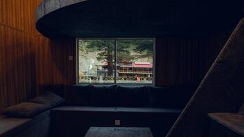 Un intérieur moderne avec une structure en pierre aux lignes courbes, des murs en bois et un espace salon offrant une vue sur un bâtiment à l’extérieur.