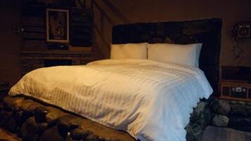 Una cama con ropa blanca, una pared de piedra y un cabecero de madera.