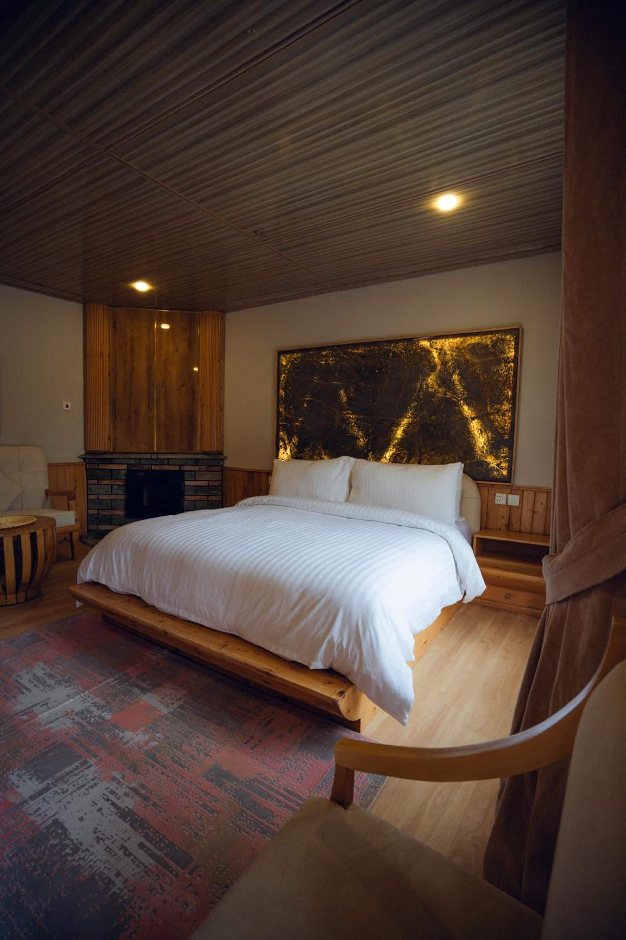 A bedroom with a large bed, wooden headboard, a fireplace, and a large abstract painting on the wall.