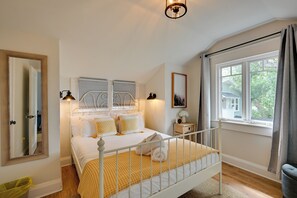 A bedroom with a white bed, a wooden floor, a window with curtains, and a wall-mounted light fixture. - 4BR Tampa Home, Easy Access to Dtwn (Tampa)