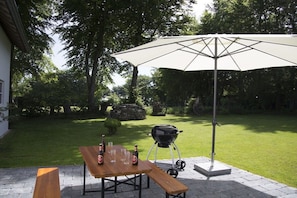 Eine Terrassengruppe im Freien mit Esstisch, Grill und einer großen Sonnenschirm, die Schatten spendet.