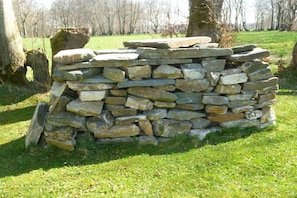 Eine Mauer aus Stein in einer grünen Umgebung, Bäume im Hintergrund.