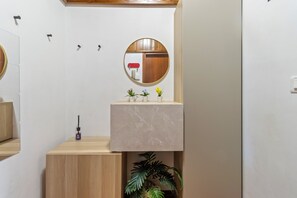 Een badkamer met een houten wastafelmeubel, een marmeren wastafel, een spiegel en een plant in een pot.