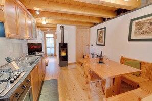 A cozy kitchen with a wood stove, a dining table with chairs, and a TV displaying 'NETFLIX'. - Borgo Nuovo Deluxe con Disney+, 2 Parcheggi (Forni di Sopra)