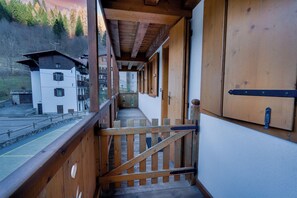 A wooden staircase leading to a balcony with a view of a building and a body of water. - Borgo Nuovo Deluxe con Disney+, 2 Parcheggi (Forni di Sopra)