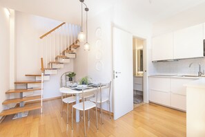 Een moderne keuken met witte kasten, een houten trap en een eethoek met een tafel en stoelen.