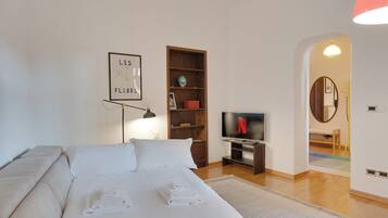 A bedroom with a bed, a desk, a TV, a bookshelf, and a framed picture on the wall.