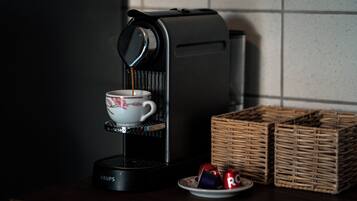 Una macchina da caffè con una tazza e un piattino, un piatto con una lattina e una tazza, e due cesti di vimini su un piano di lavoro scuro.
