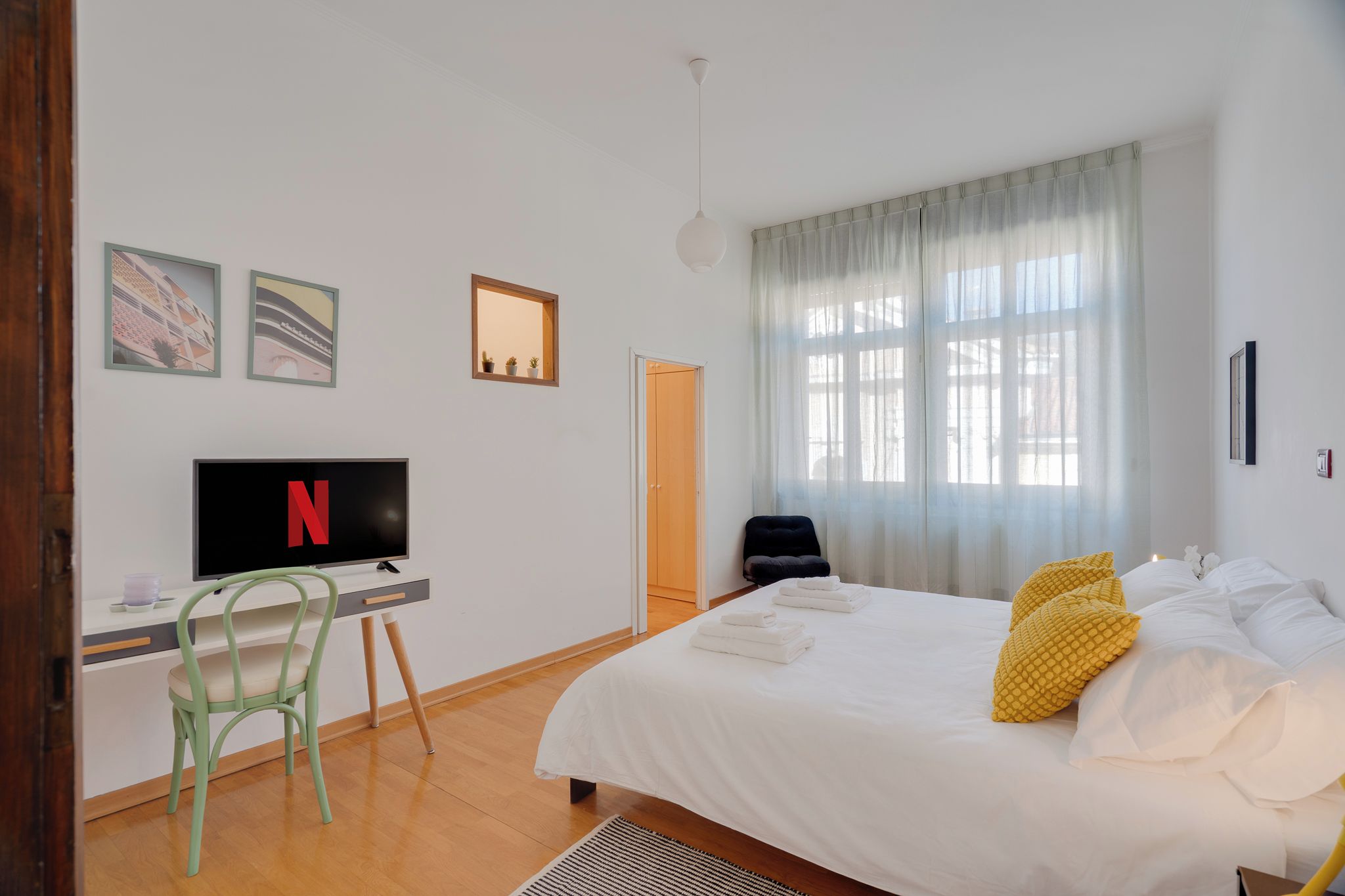 Una camera d'albergo con un letto, una scrivania con televisione, una sedia e una finestra con tende.