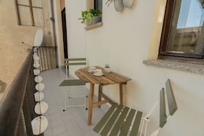 A small outdoor seating area with a table and chairs, a potted plant, and a window. - Chromatica - di Fronte a Galleria Bomb (Gorizia)