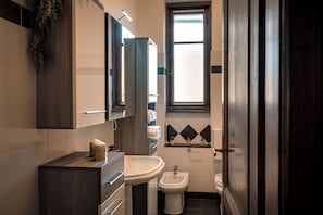A compact bathroom with a wooden vanity, a white sink, a bidet, and a window with frosted glass. - Chromatica - di Fronte a Galleria Bomb (Gorizia)