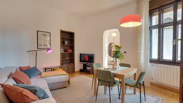 Ein modernes Wohnzimmer mit einer Couch, einem Esstisch mit Stühlen, einem Fernseher und einem Bücherregal.