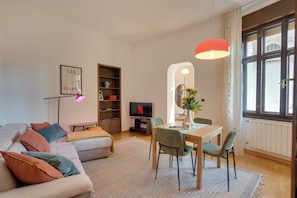 A modern living room with a sofa, a dining table with chairs, a TV, and a bookshelf. - Chromatica - di Fronte a Galleria Bomb (Gorizia)