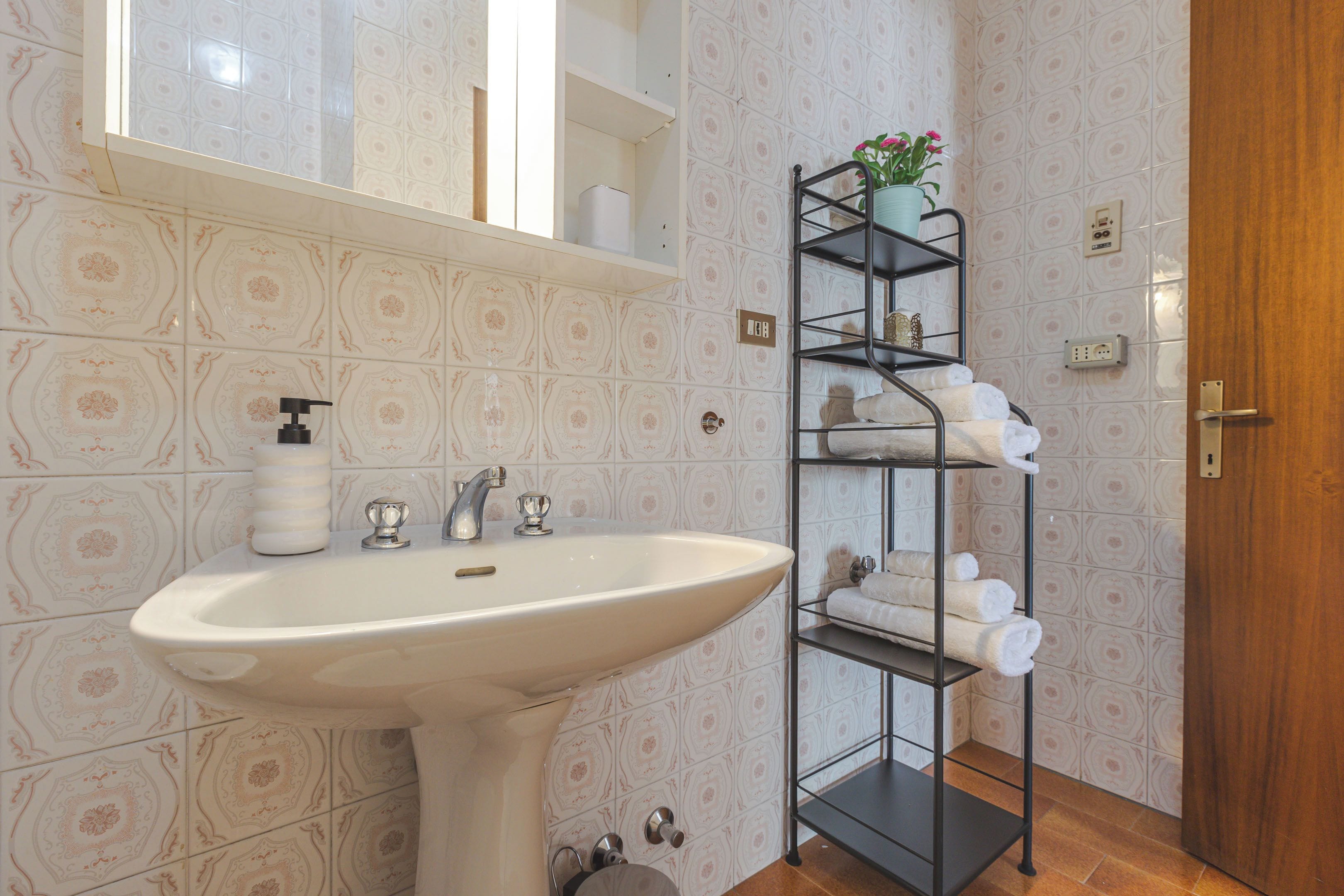 Un baño con lavamanos blanco, espejo, toallero y baldosas estampadas.