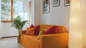 A living room with a sofa, pillows, a plant, and framed pictures on the wall.