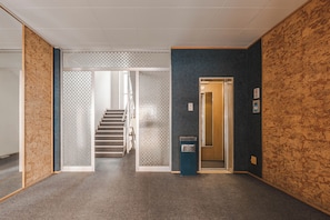 Un pasillo con piso alfombrado, una escalera y una puerta que da a otra habitación.