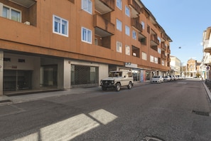 Eine Straße mit einer Reihe geparkter Autos und einem Gebäude mit vielen Fenstern und Balkonen.