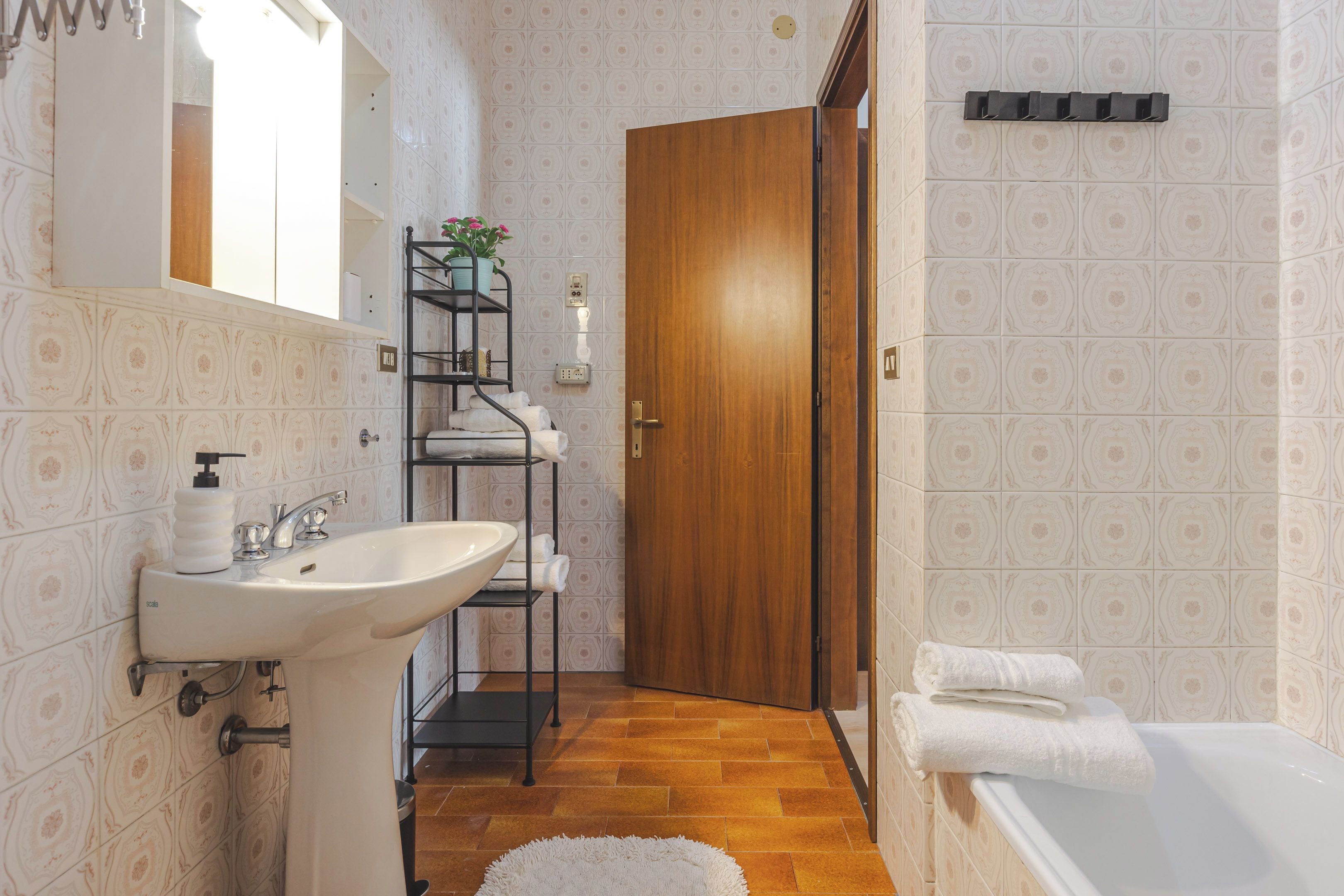 Un bagno con un lavandino, una porta in legno, uno scaffale con asciugamani e una vasca da bagno.