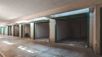 A corridor with open doors leading to rooms, a concrete floor, and a ceiling with visible beams.