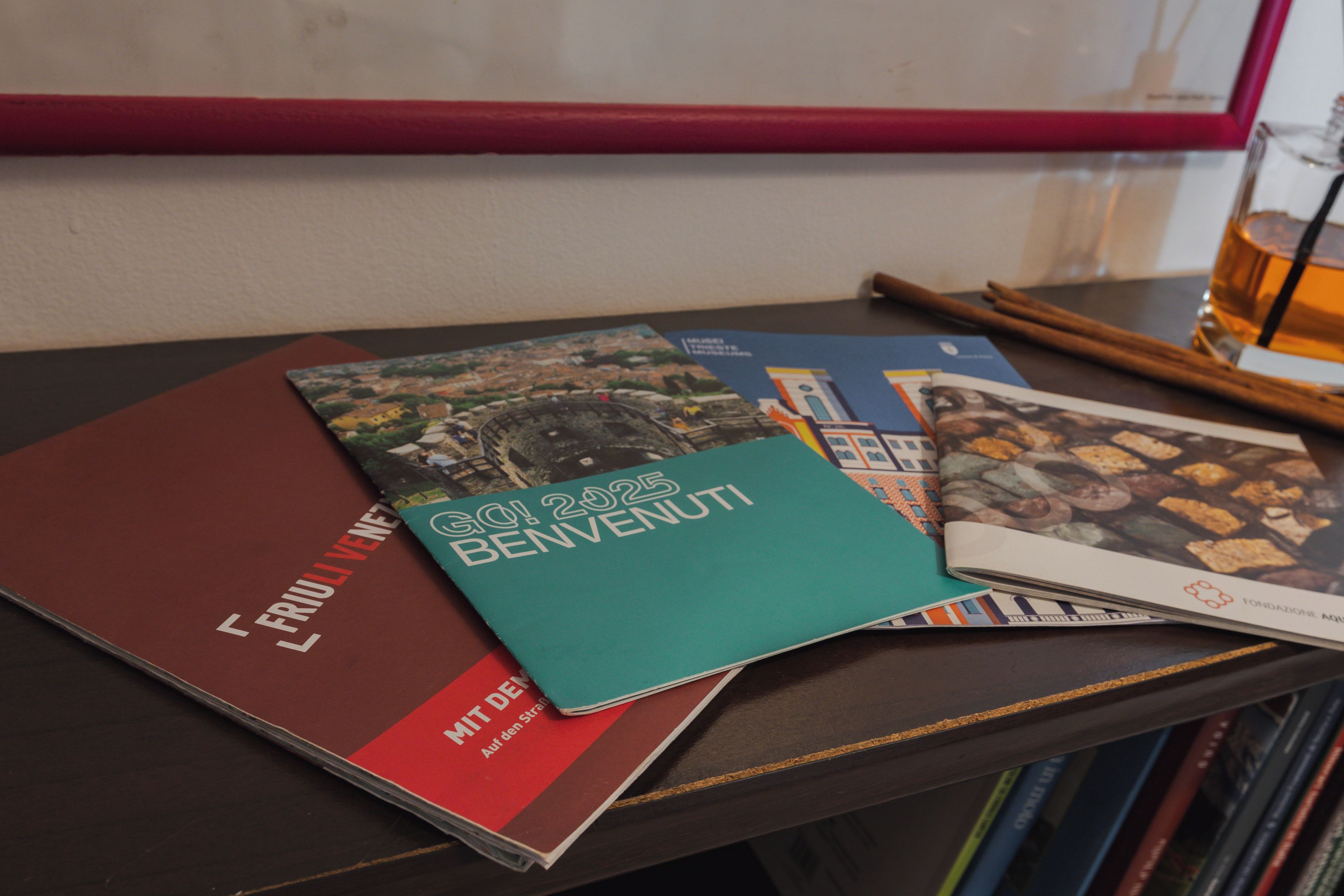 A stack of books on a table with a framed picture in the background.