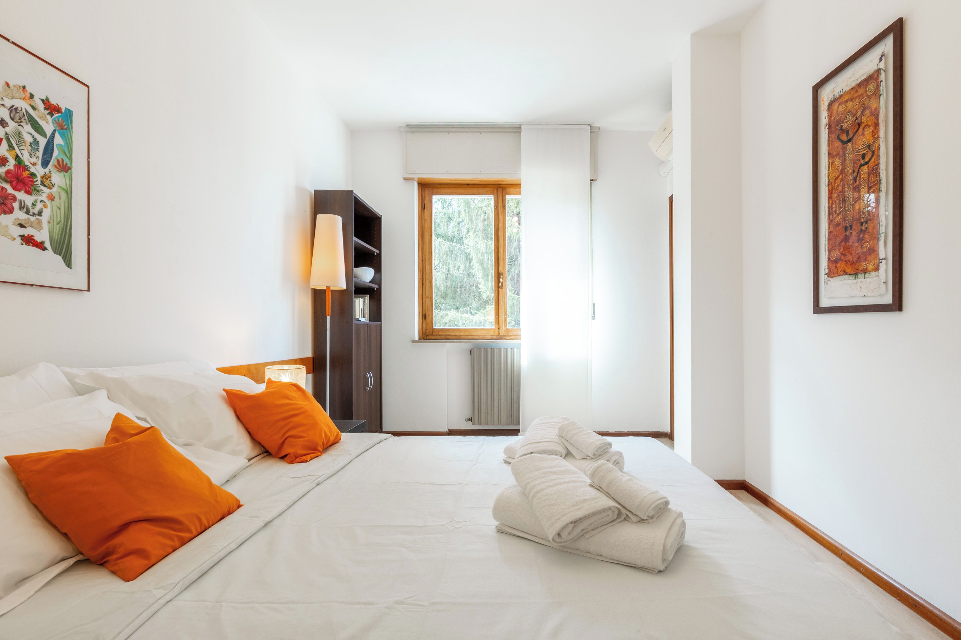 A hotel room with a bed, a nightstand, a wardrobe, a window, and a framed picture on the wall.