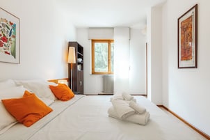 Una habitación de hotel con una cama, una mesita de noche, un armario, una ventana y un cuadro en la pared.