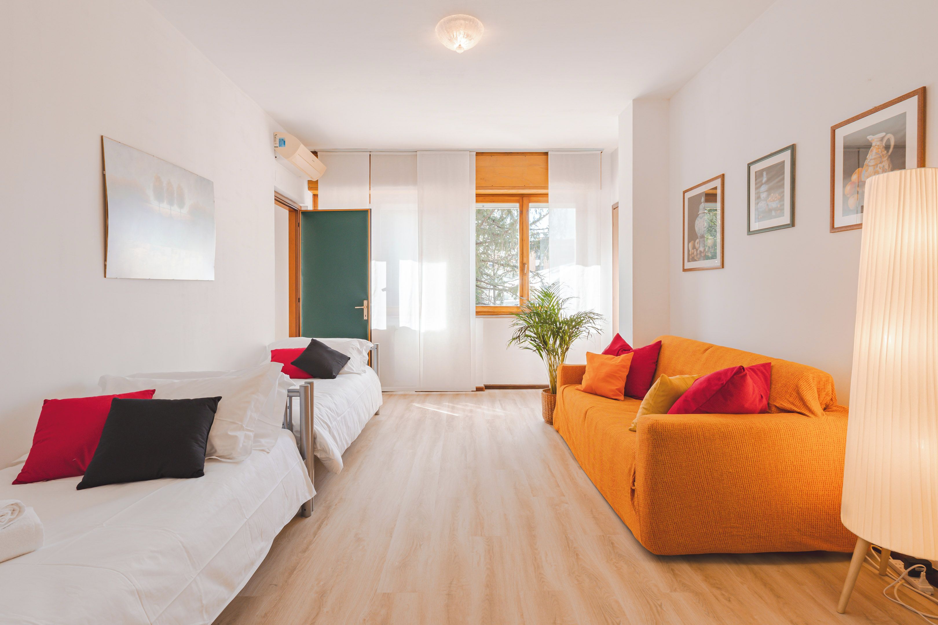 A hotel room with a bed, a sofa, a desk, a window, and a plant.