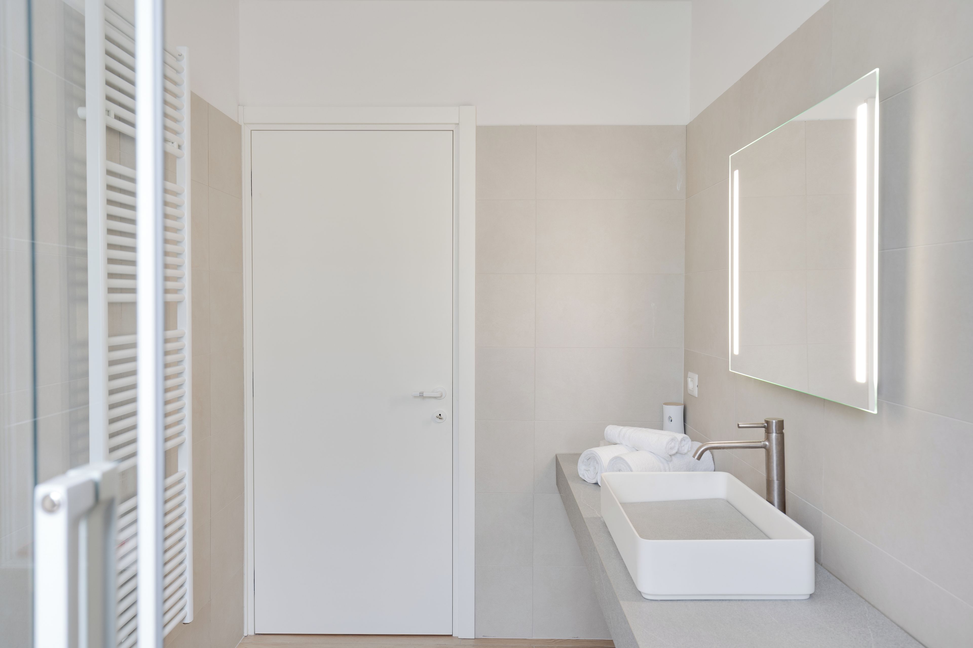 Un bany modern amb un rentamans blanc, un mirall i una porta.