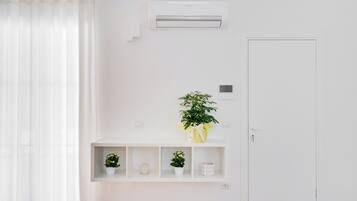 A minimalist room with a white door, an air conditioning unit, a shelf with potted plants, and a white curtain.