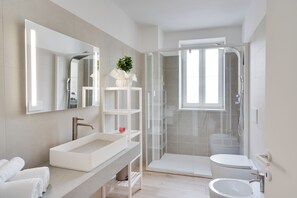 Un baño moderno con cabina de ducha de vidrio, un lavabo blanco y un espejo grande.