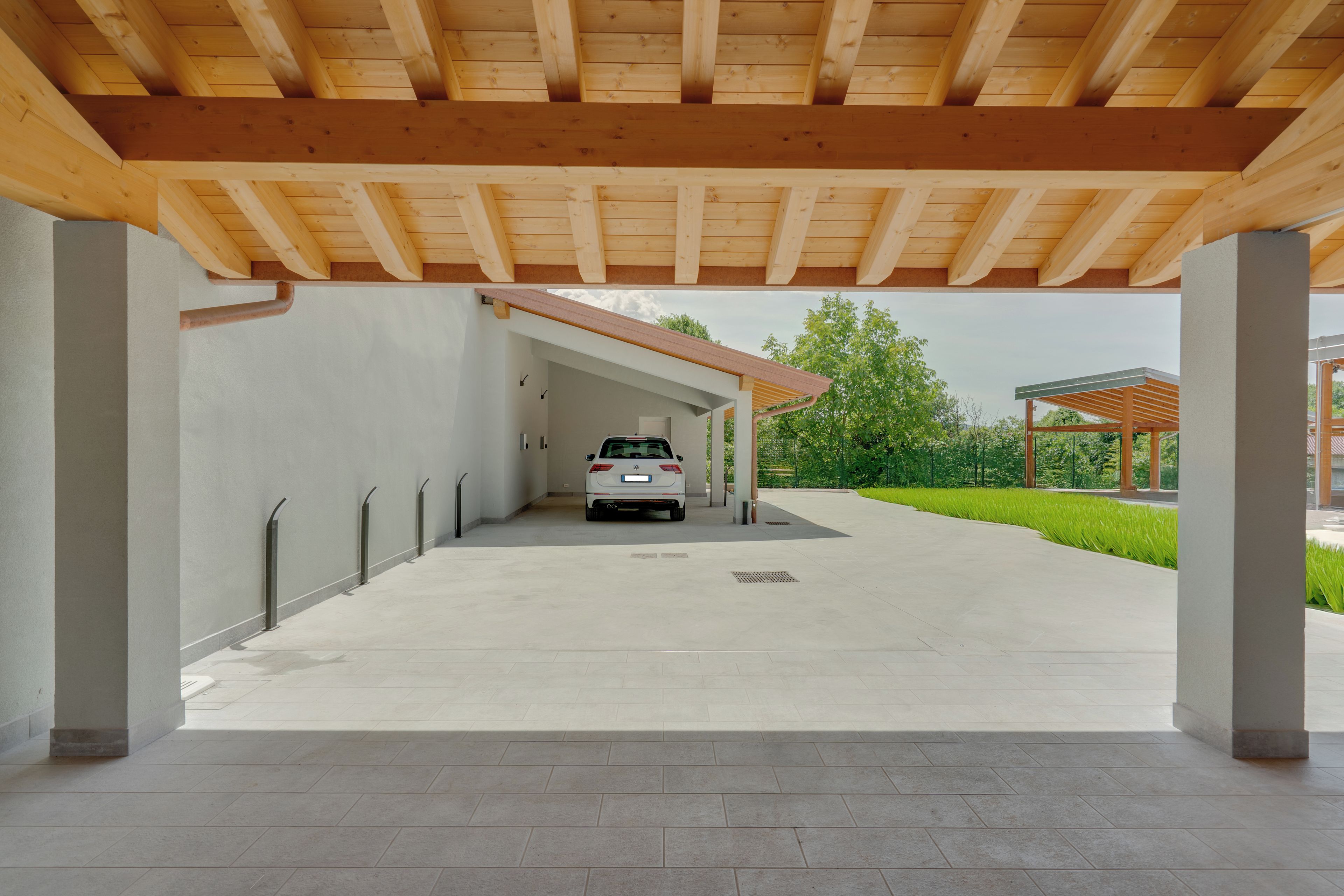 A covered parking area with a white car parked under a wooden beam structure.