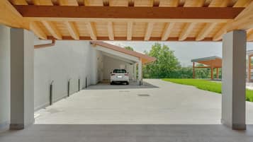 A covered parking area with a white car parked under a wooden beam structure.