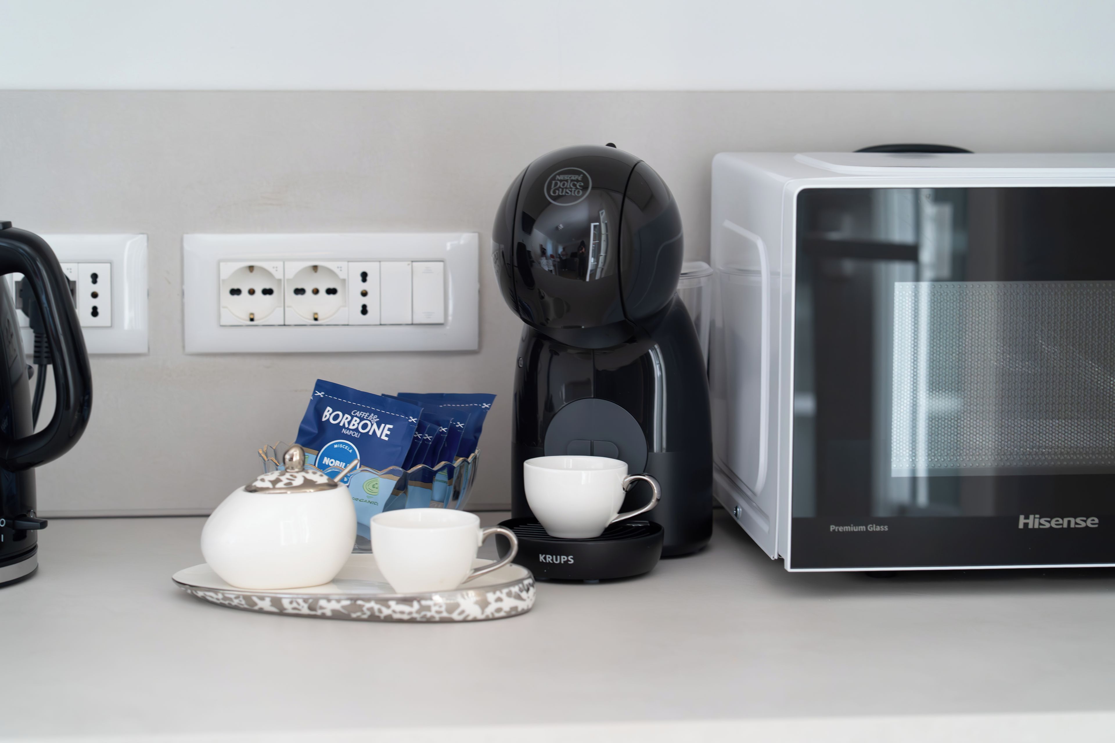 Une petite cuisine équipée d’une machine à café, d’un four à micro-ondes et d’un support pour les capsules de café.