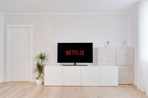 Una sala moderna con una unidad de entretenimiento blanca, un televisor de pantalla plana mostrando 'NETFLIX' y una pequeña planta en maceta.