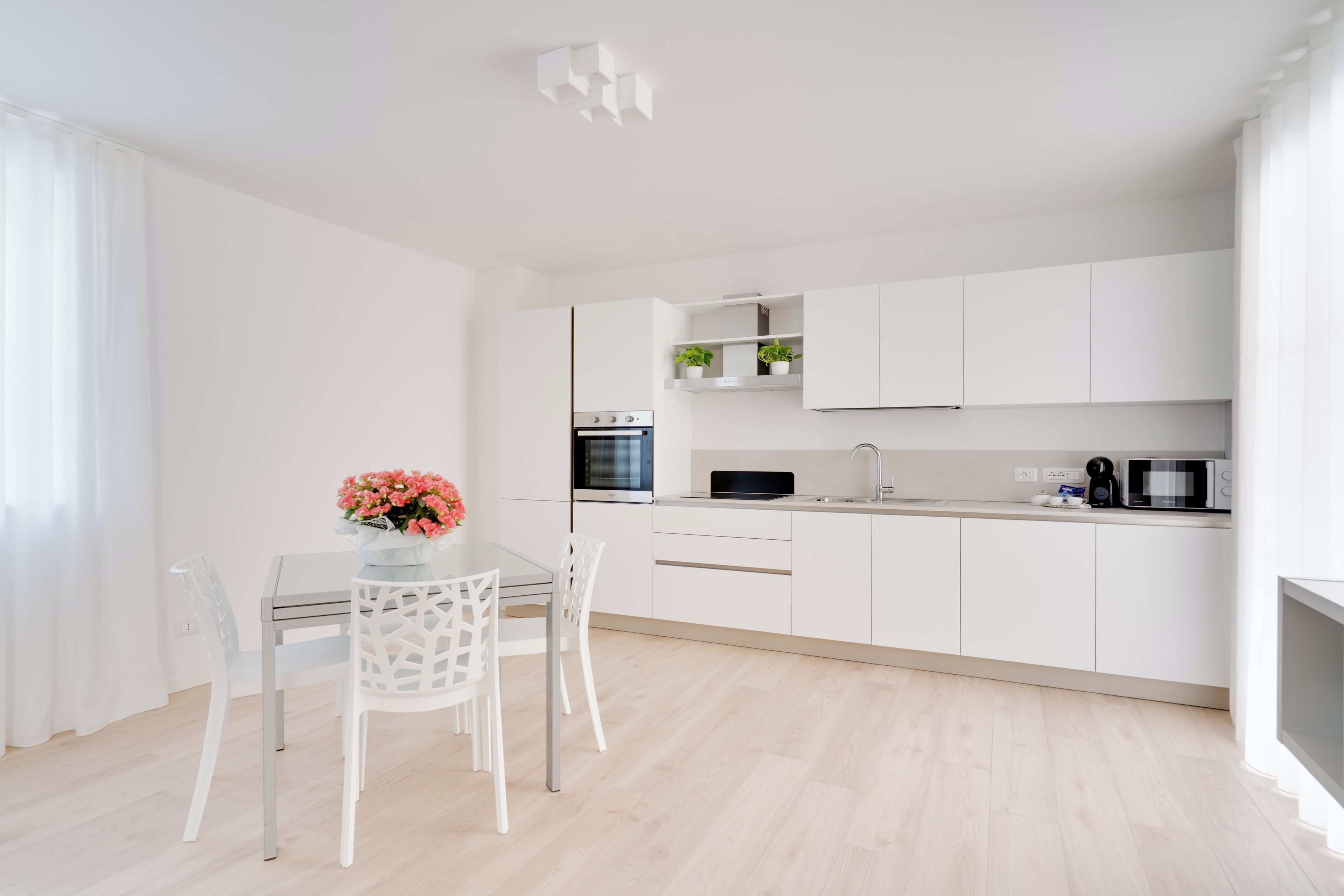 Una cocina moderna con armarios blancos, una mesa de comedor con sillas y un florero con flores.