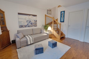 A living room with a grey sofa, a wooden cabinet, a painting, a staircase, and a door.